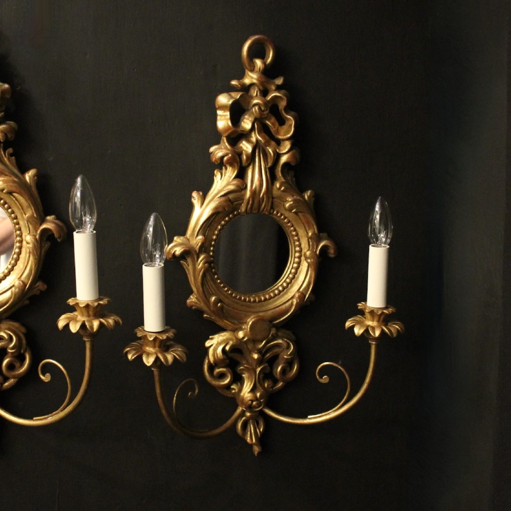 A pair of carved giltwood twin-arm girandole wall sconces featuring central circular mirrors, ornate scrollwork, and bow-tied cresting. View II