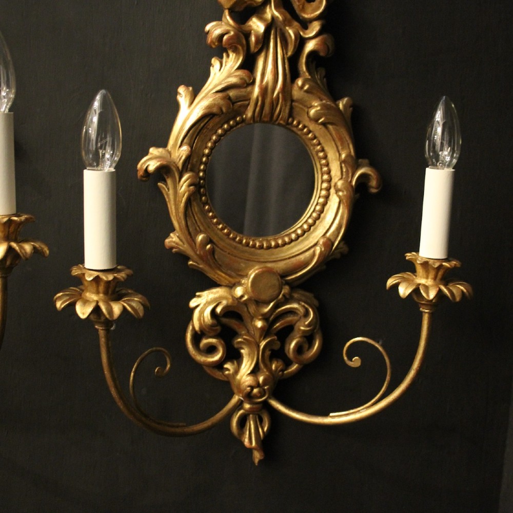 A pair of carved giltwood twin-arm girandole wall sconces featuring central circular mirrors, ornate scrollwork, and bow-tied cresting. View III