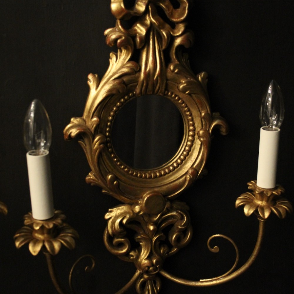 A pair of carved giltwood twin-arm girandole wall sconces featuring central circular mirrors, ornate scrollwork, and bow-tied cresting. View IV