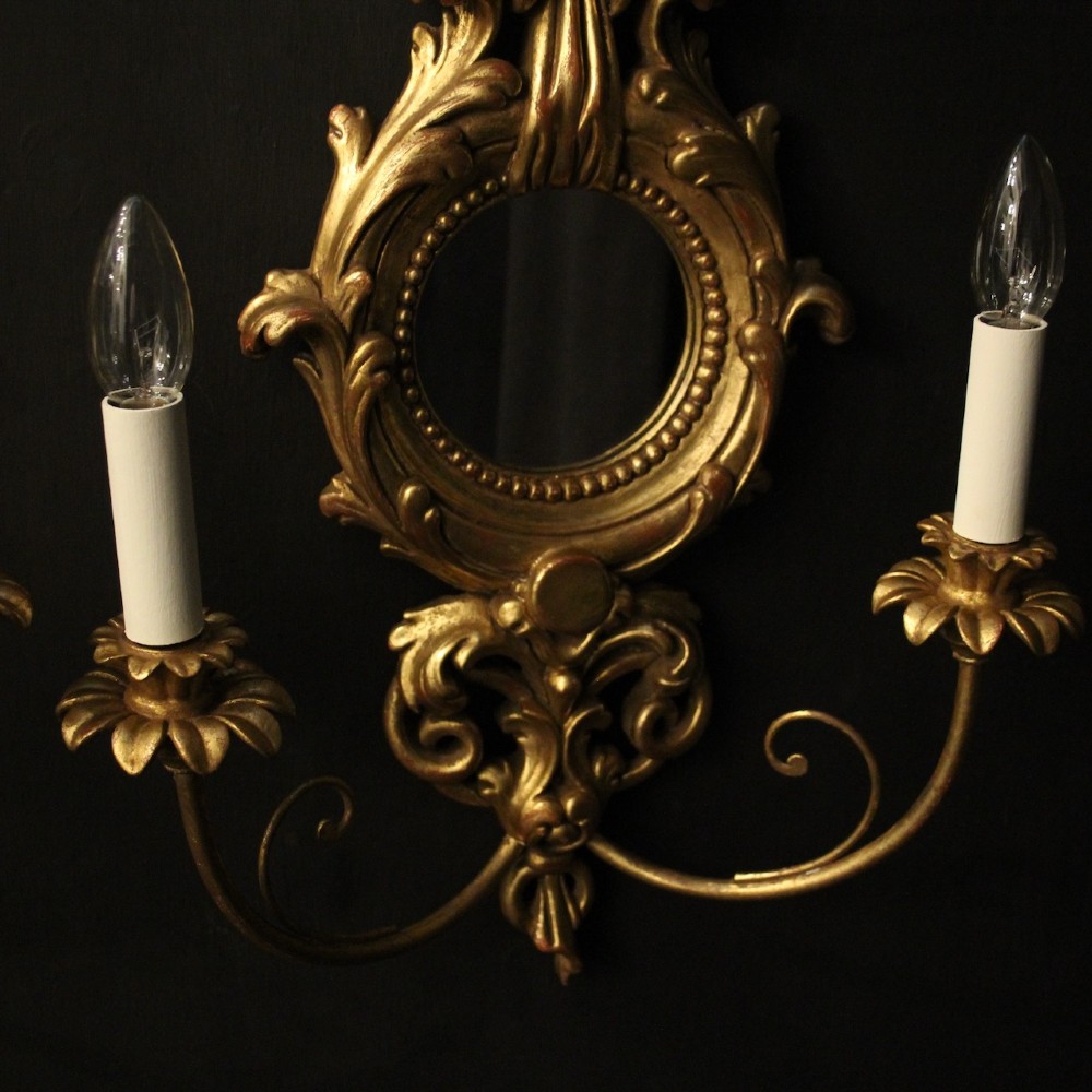 A pair of carved giltwood twin-arm girandole wall sconces featuring central circular mirrors, ornate scrollwork, and bow-tied cresting. View VII