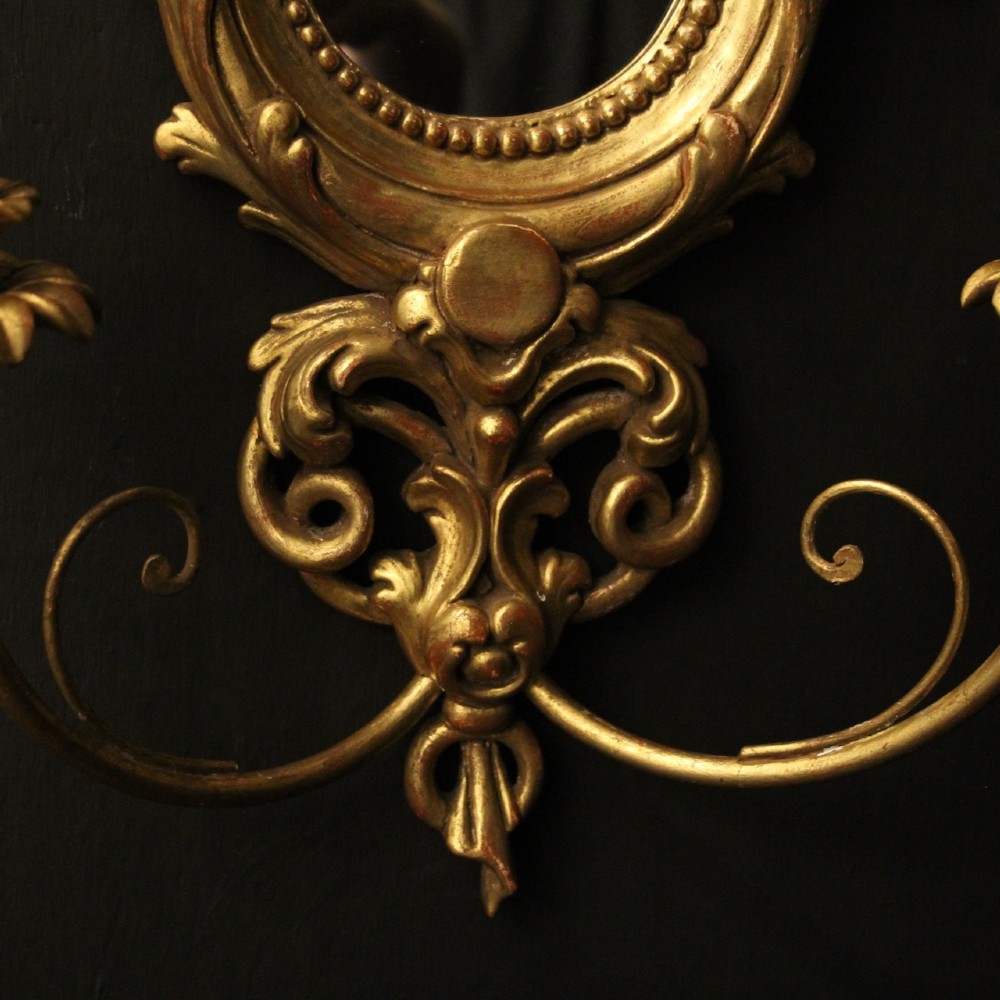 A pair of carved giltwood twin-arm girandole wall sconces featuring central circular mirrors, ornate scrollwork, and bow-tied cresting. View IX