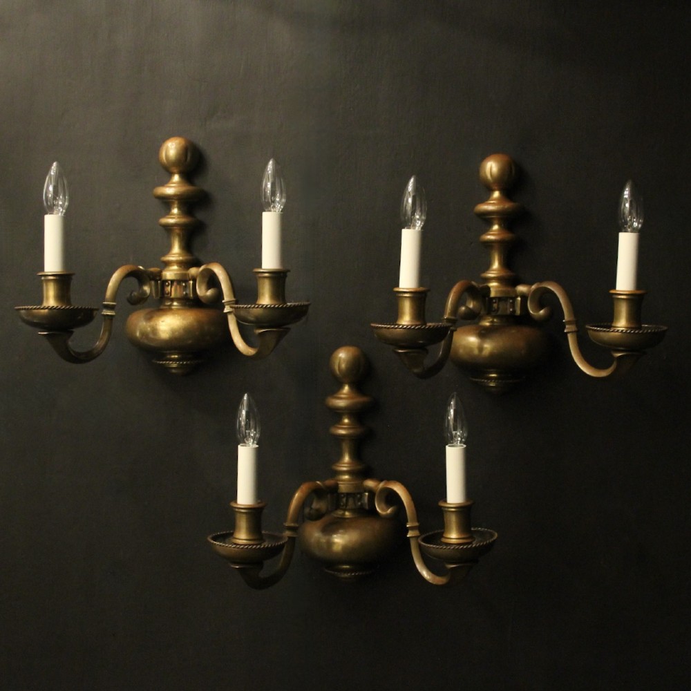 A set of three antique bronze wall sconces, each featuring a turned central baluster and two scrolled arms holding candle-style bulb holders.