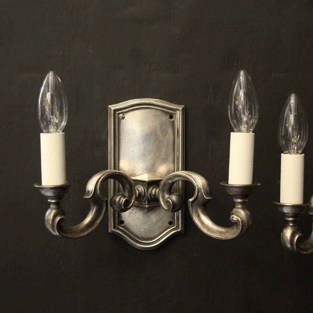 A pair of antique silver-plated twin-branch wall sconces featuring scrolling arms and moulded backplates against a dark background. View II