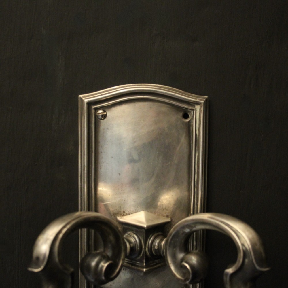 A pair of antique silver-plated twin-branch wall sconces featuring scrolling arms and moulded backplates against a dark background. View IV
