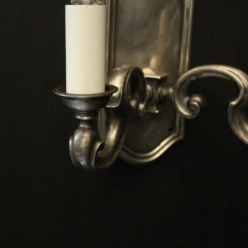 A pair of antique silver-plated twin-branch wall sconces featuring scrolling arms and moulded backplates against a dark background. View VI