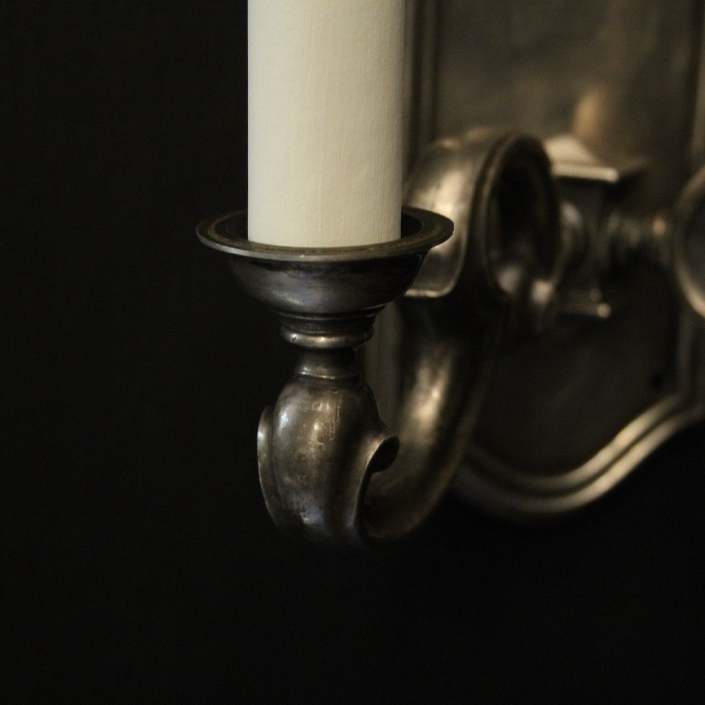 A pair of antique silver-plated twin-branch wall sconces featuring scrolling arms and moulded backplates against a dark background. View VII