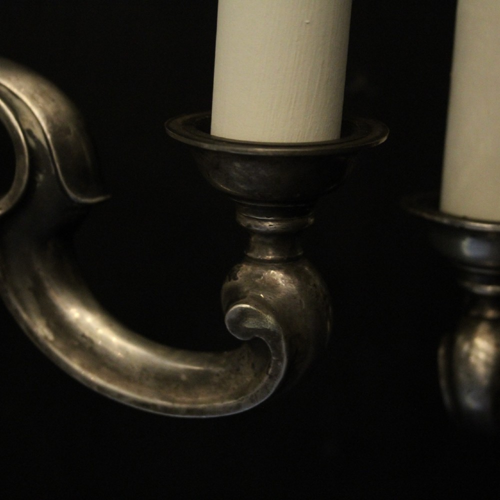 A pair of antique silver-plated twin-branch wall sconces featuring scrolling arms and moulded backplates against a dark background. View VIII