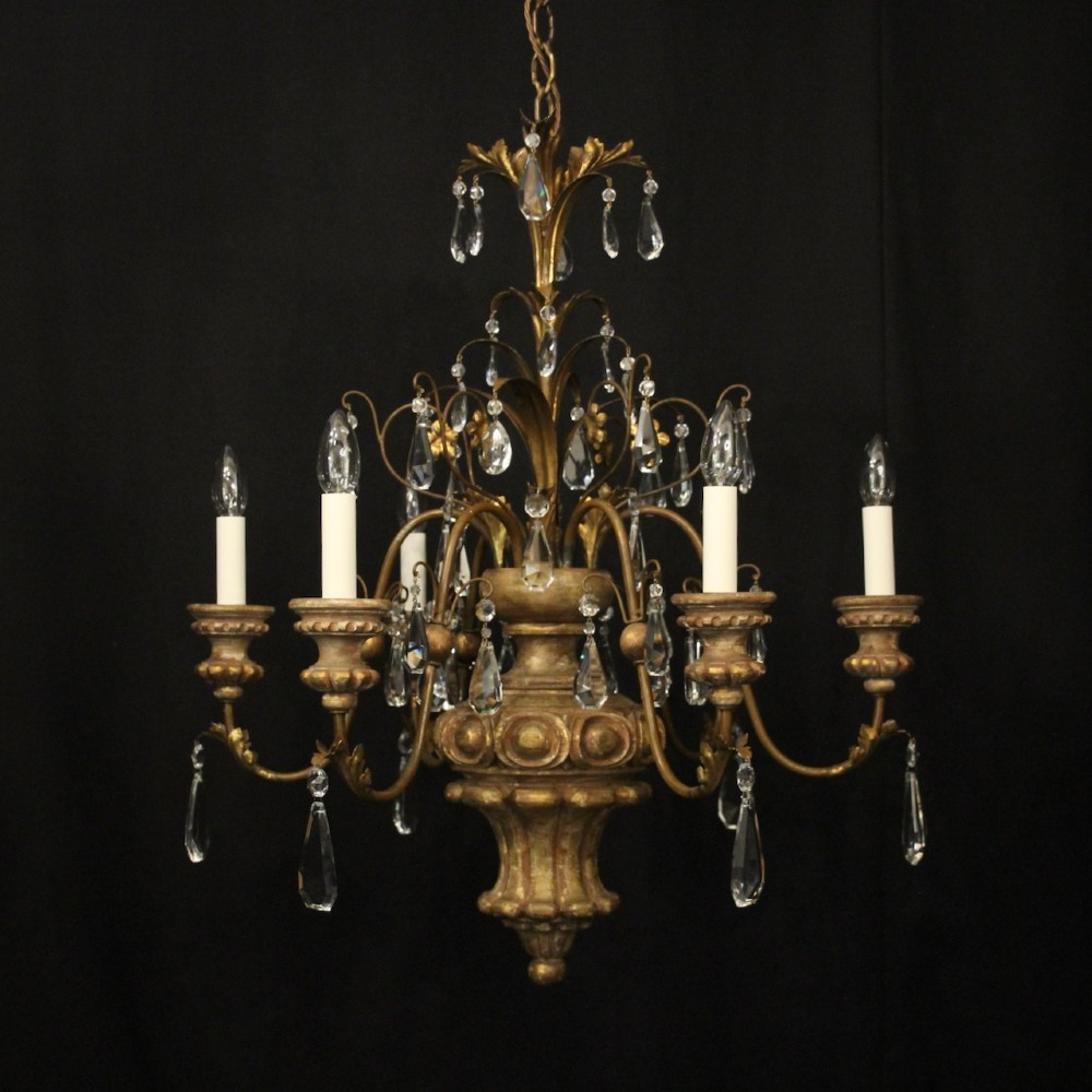 An antique Italian Florentine six-arm chandelier featuring gilded scrolling branches, a carved central column, white candle sleeves, and hanging crystal droplets.
