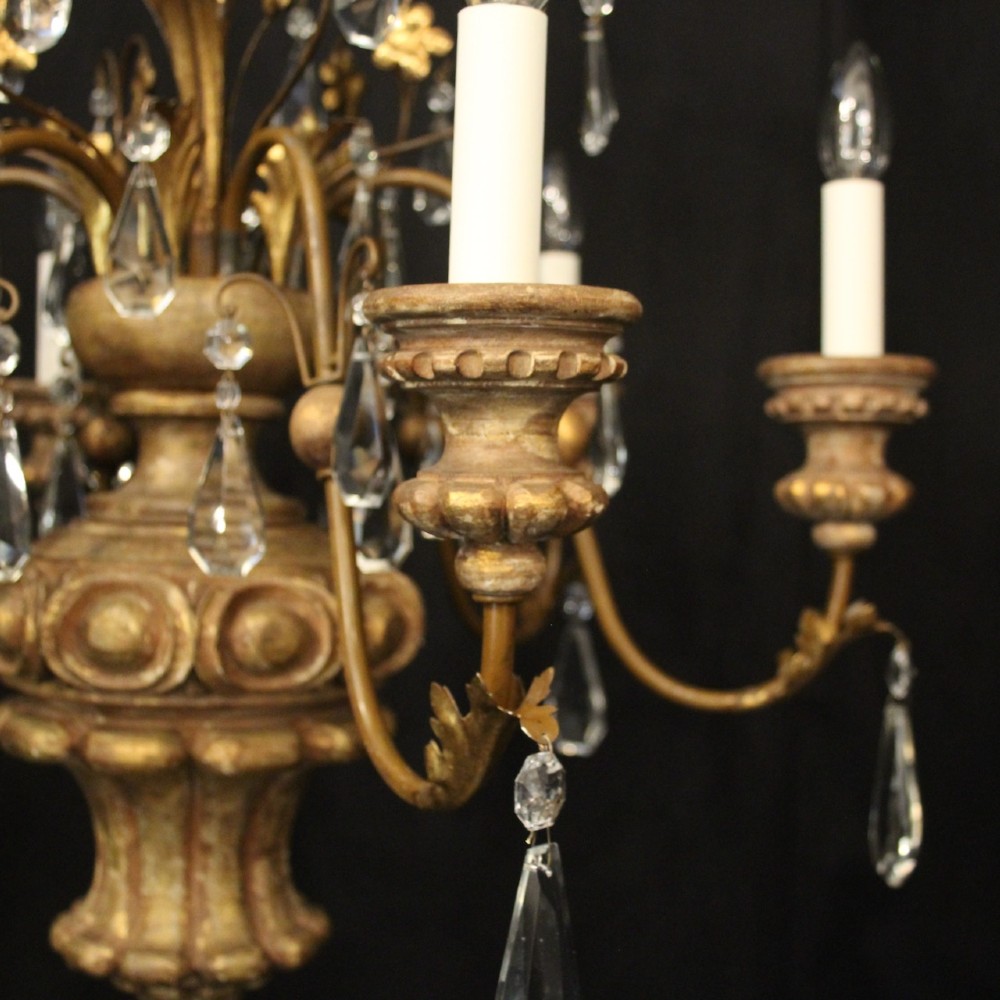 An antique Italian Florentine six-arm chandelier featuring gilded scrolling branches, a carved central column, white candle sleeves, and hanging crystal droplets. View IV