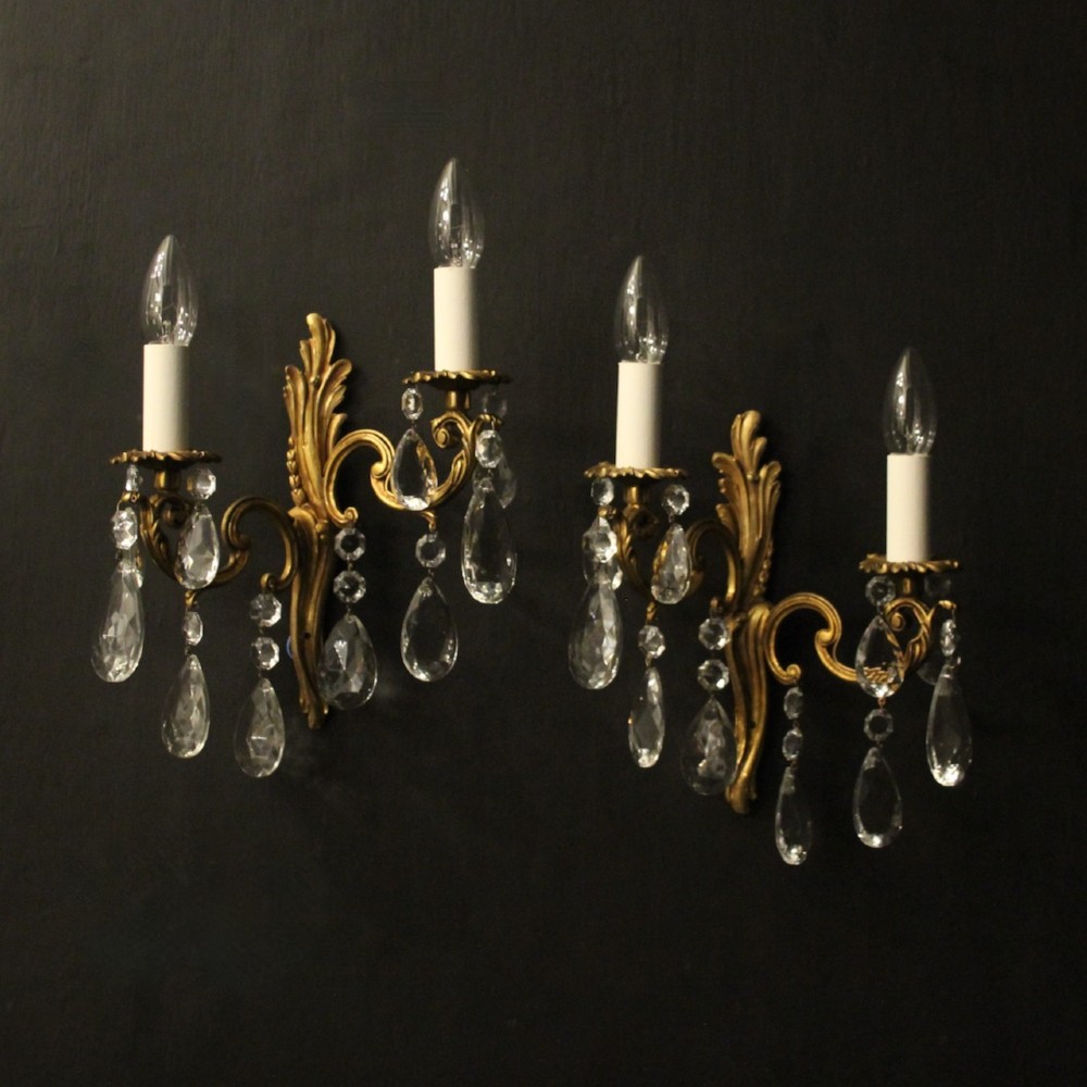A pair of antique French gilt metal twin-arm wall sconces decorated with cut crystal teardrop pendants.