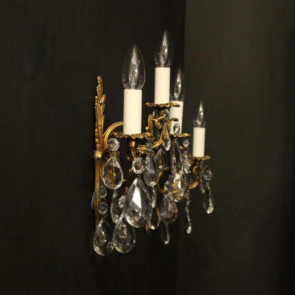 A pair of antique French gilt metal twin-arm wall sconces decorated with cut crystal teardrop pendants. View X