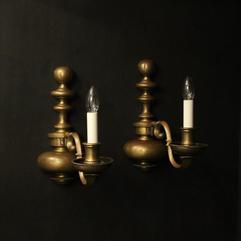 A pair of antique bronze single-arm wall lights with turned baluster shafts and candle-style fittings against a dark background.