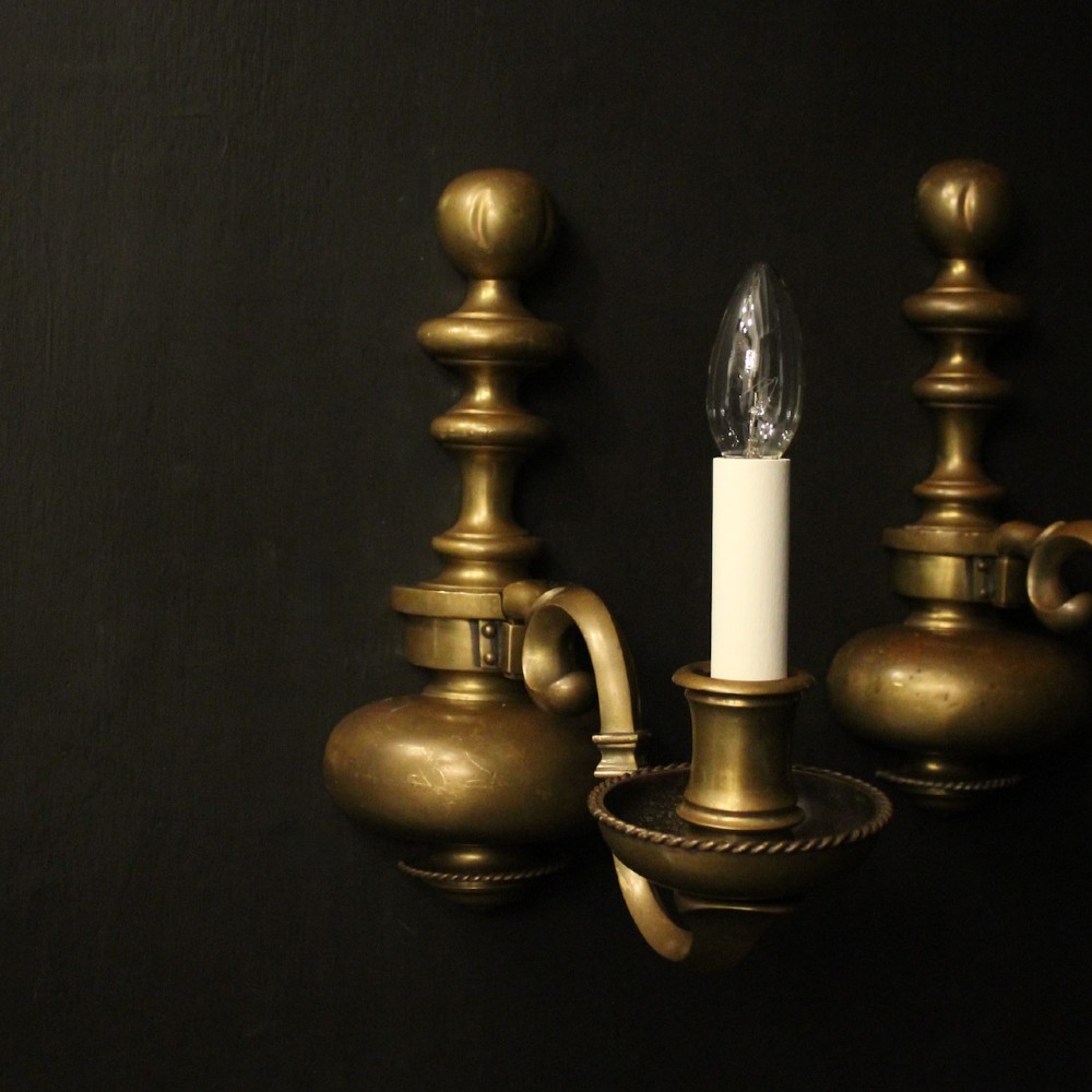 A pair of antique bronze single-arm wall lights with turned baluster shafts and candle-style fittings against a dark background. View II