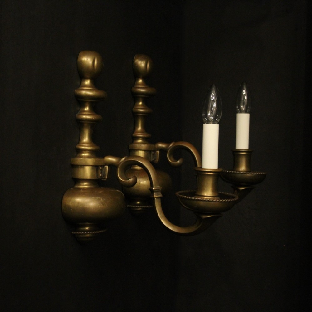 A pair of antique bronze single-arm wall lights with turned baluster shafts and candle-style fittings against a dark background. View X