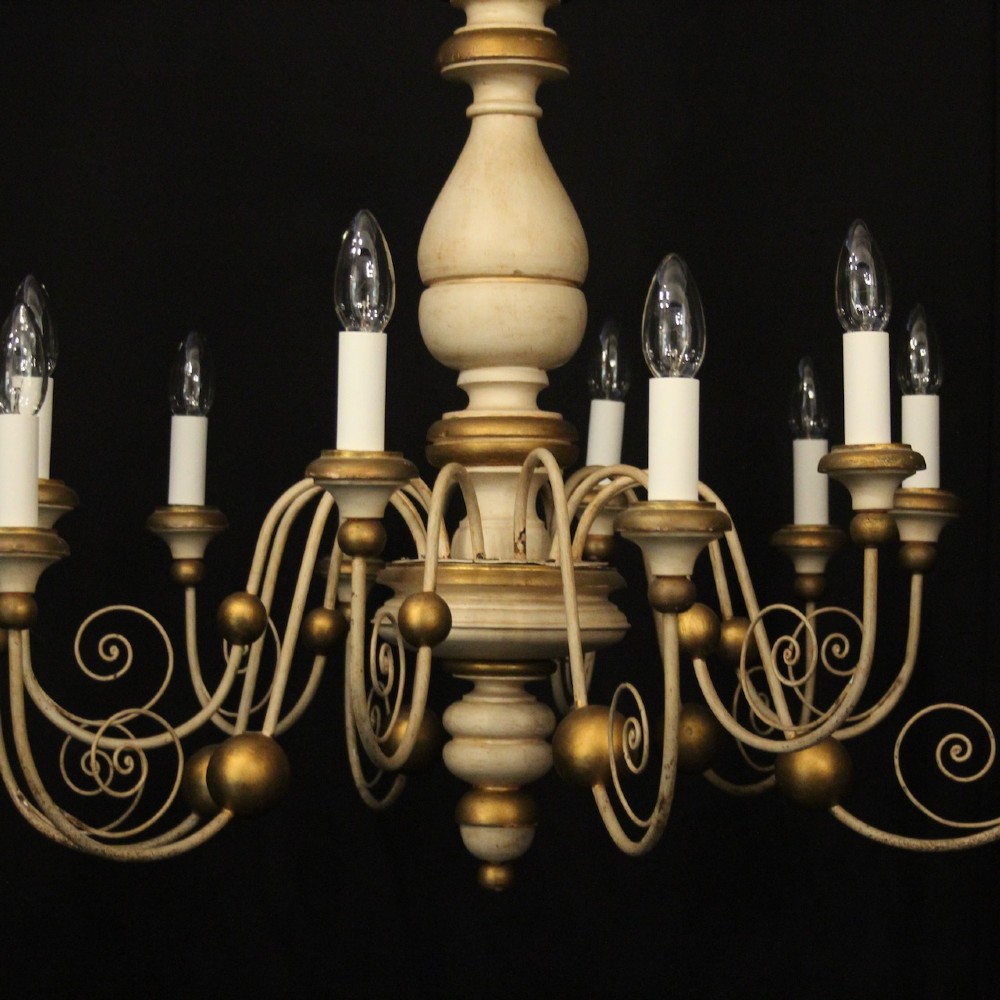 A twelve-light Florentine style ceiling chandelier featuring a cream and gilded turned wooden central column with wrought scrollwork branch arms and candle sleeves. View II
