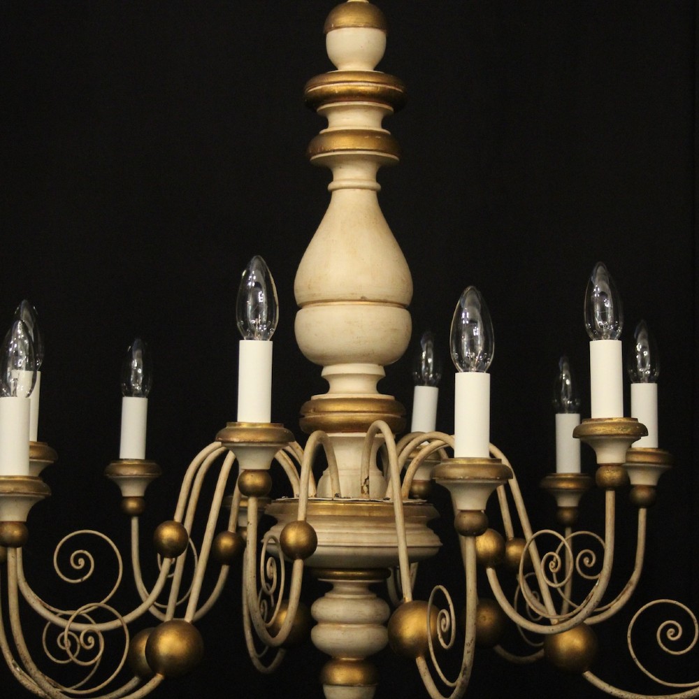 A twelve-light Florentine style ceiling chandelier featuring a cream and gilded turned wooden central column with wrought scrollwork branch arms and candle sleeves. View III