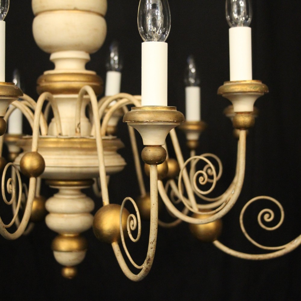 A twelve-light Florentine style ceiling chandelier featuring a cream and gilded turned wooden central column with wrought scrollwork branch arms and candle sleeves. View IV