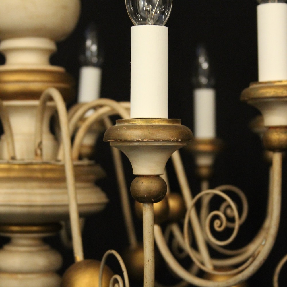 A twelve-light Florentine style ceiling chandelier featuring a cream and gilded turned wooden central column with wrought scrollwork branch arms and candle sleeves. View V