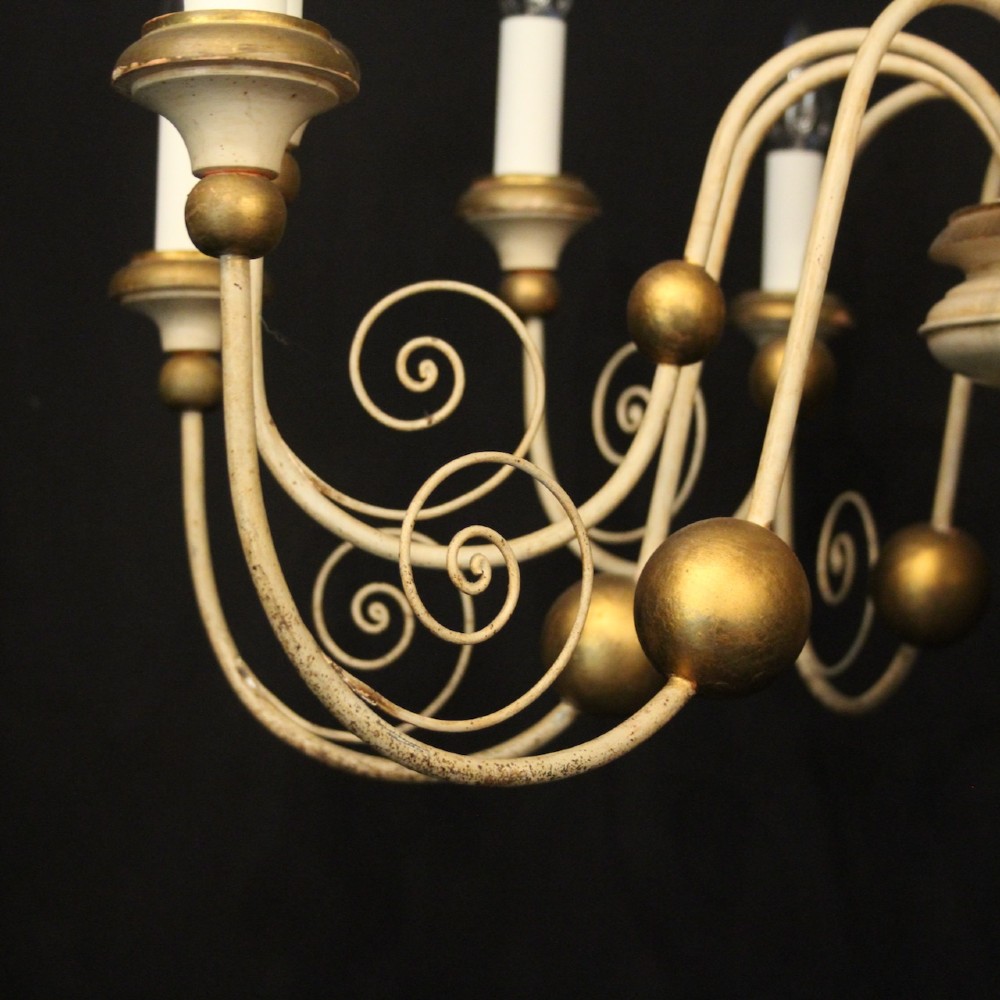 A twelve-light Florentine style ceiling chandelier featuring a cream and gilded turned wooden central column with wrought scrollwork branch arms and candle sleeves. View VI