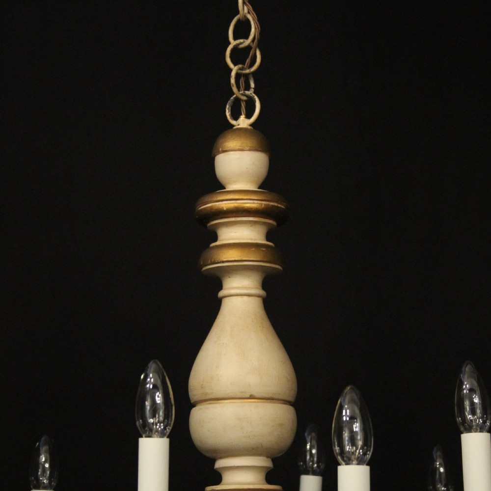 A twelve-light Florentine style ceiling chandelier featuring a cream and gilded turned wooden central column with wrought scrollwork branch arms and candle sleeves. View IX
