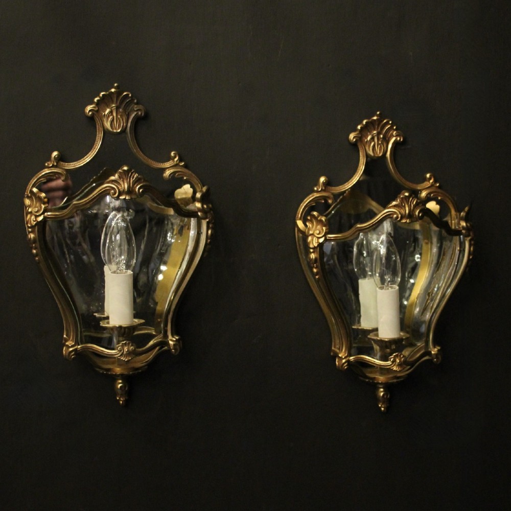 A pair of French gilded bronze half lanterns featuring curved glass panels and decorative palmette cresting, mounted as wall sconces.