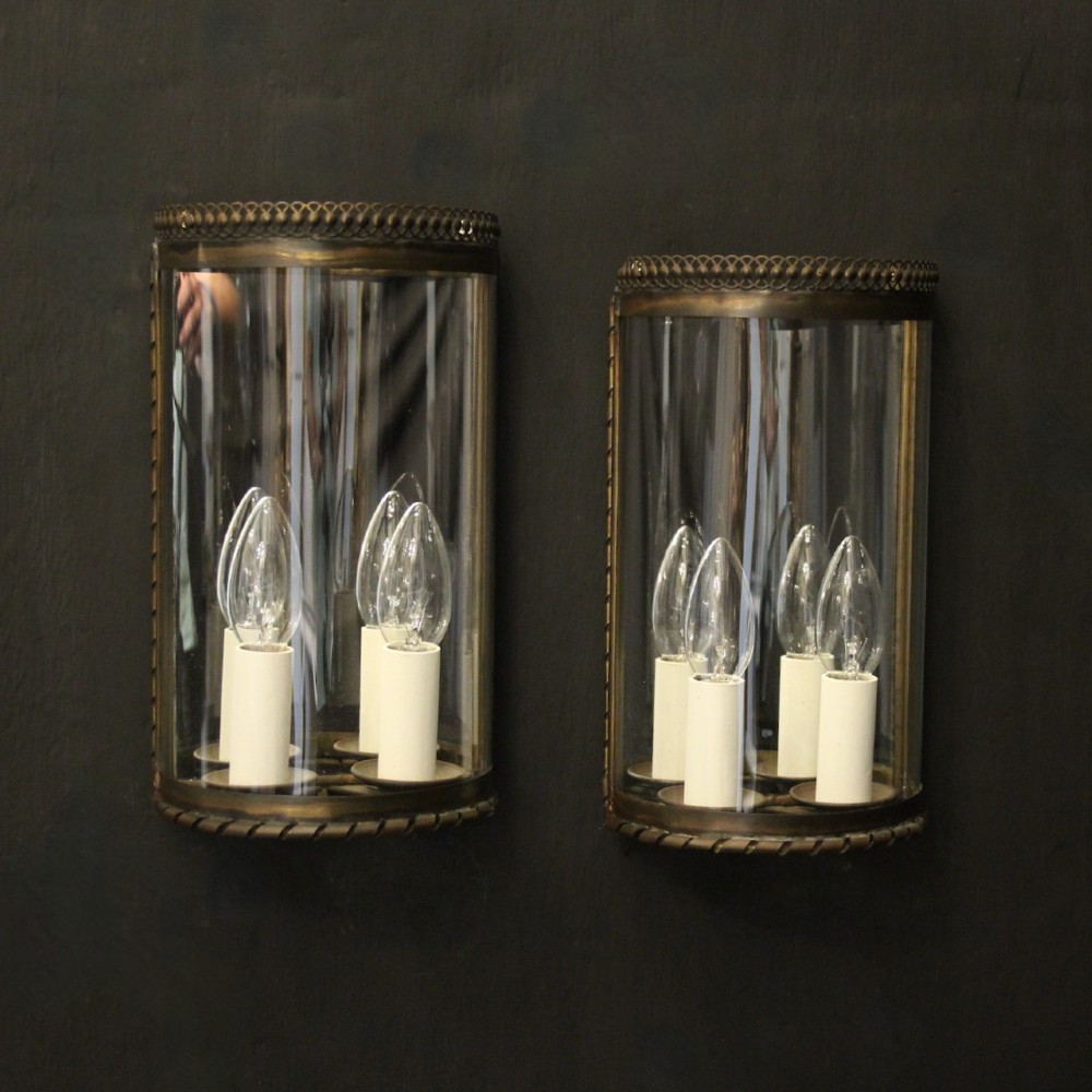 A pair of semi-circular brass half-lantern wall sconces featuring curved clear glass panels and four faux candle-bulb fittings inside each unit.