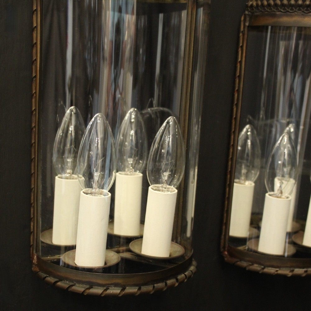 A pair of semi-circular brass half-lantern wall sconces featuring curved clear glass panels and four faux candle-bulb fittings inside each unit. View IV