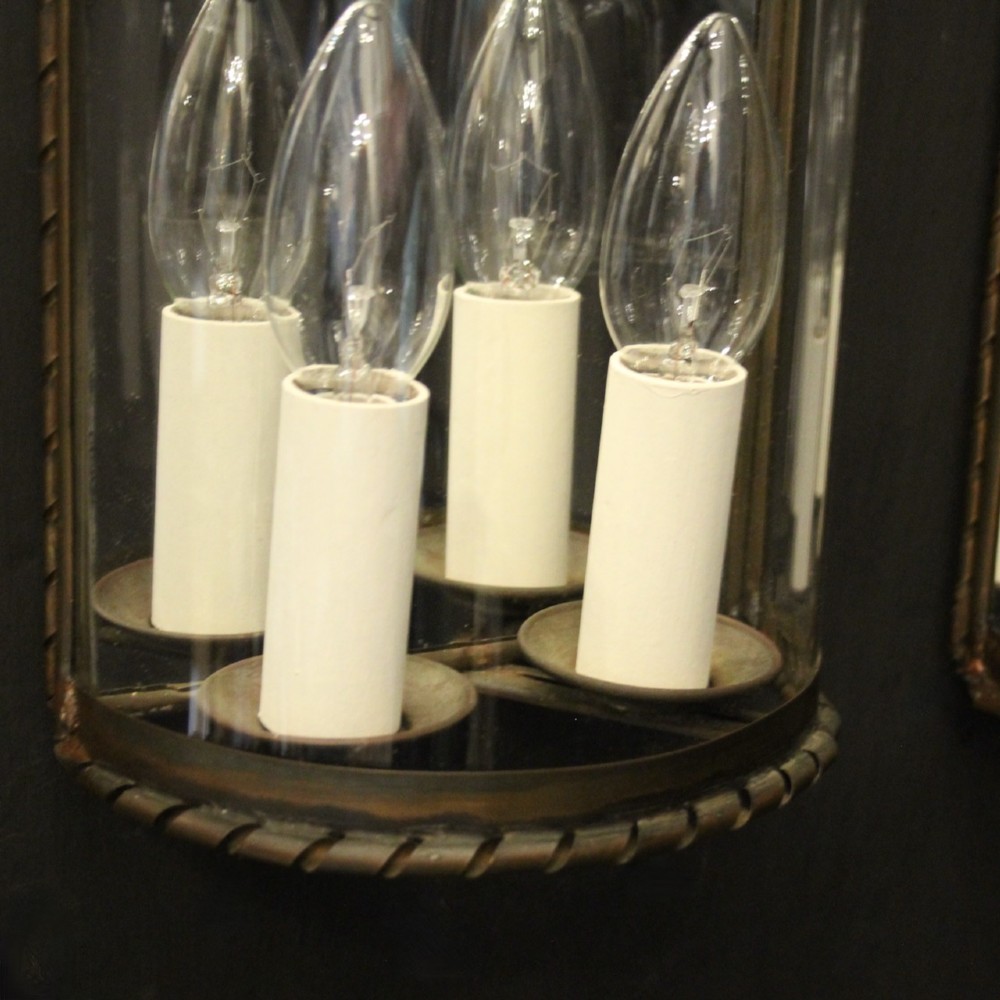 A pair of semi-circular brass half-lantern wall sconces featuring curved clear glass panels and four faux candle-bulb fittings inside each unit. View V