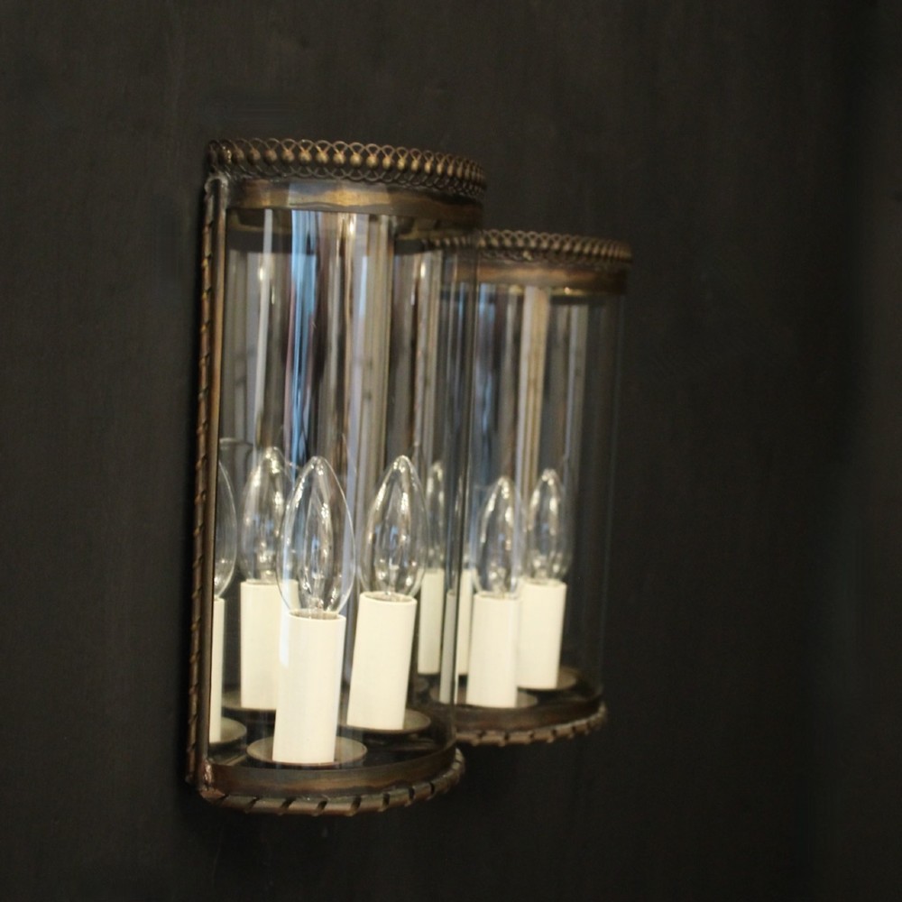 A pair of semi-circular brass half-lantern wall sconces featuring curved clear glass panels and four faux candle-bulb fittings inside each unit. View X