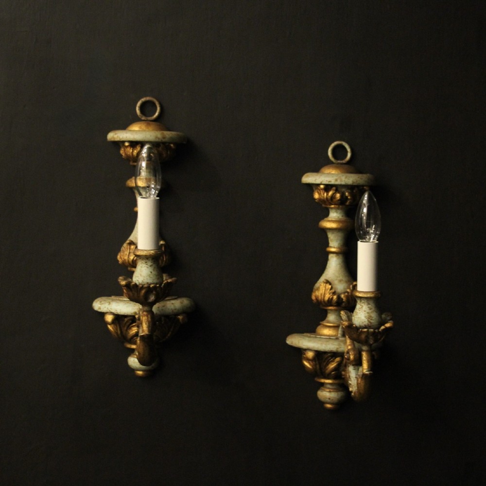 A pair of antique Italian wall lights featuring turned polychrome stems in pale green and gold with carved leaf accents and single candlestick arms.