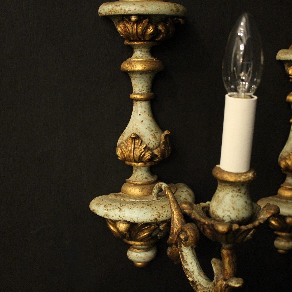 A pair of antique Italian wall lights featuring turned polychrome stems in pale green and gold with carved leaf accents and single candlestick arms. View V