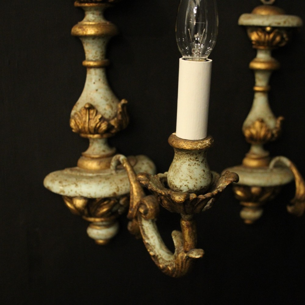 A pair of antique Italian wall lights featuring turned polychrome stems in pale green and gold with carved leaf accents and single candlestick arms. View VI