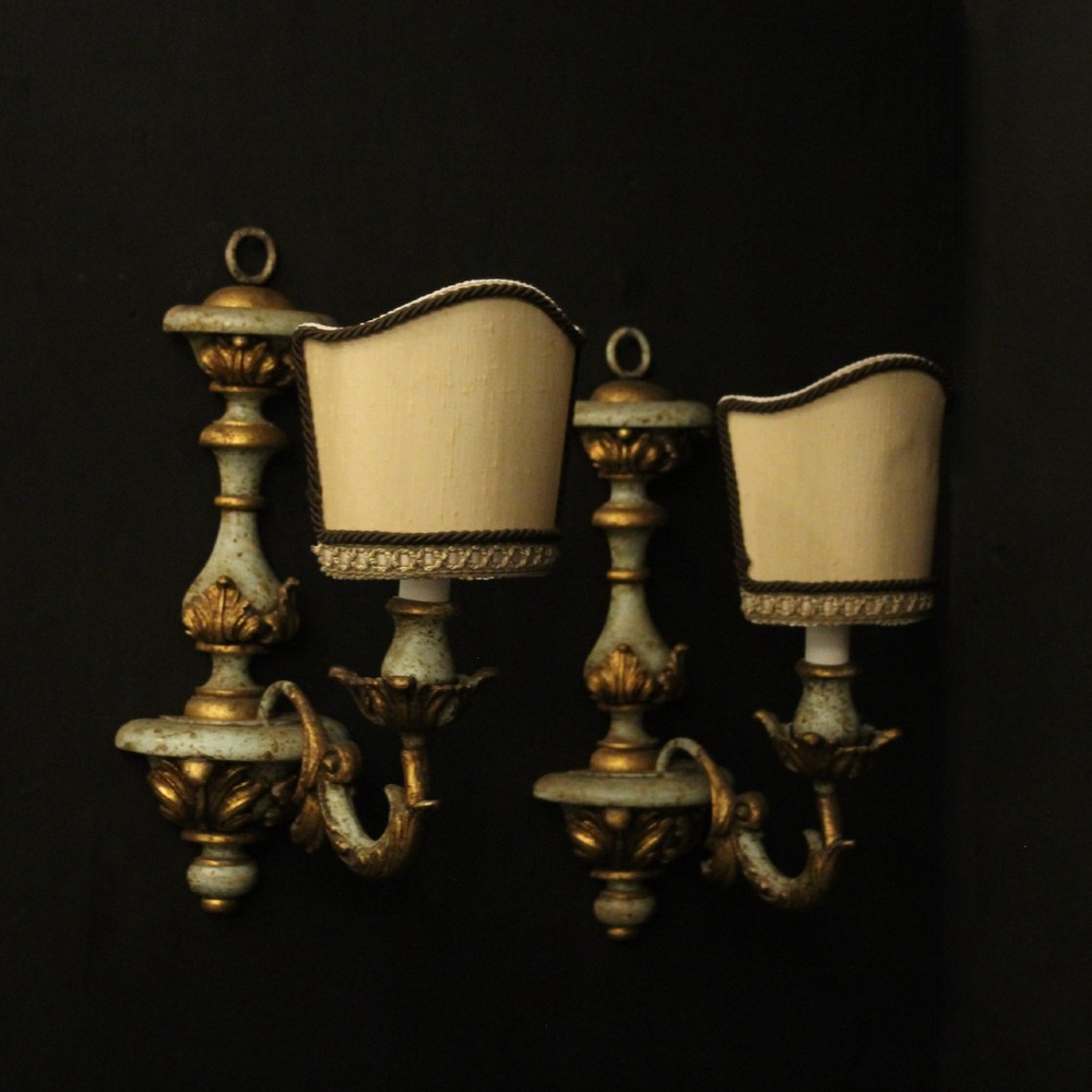 A pair of antique Italian wall lights featuring turned polychrome stems in pale green and gold with carved leaf accents and single candlestick arms. View X