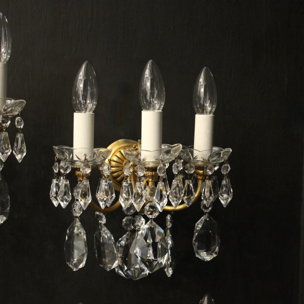 A set of four French triple-arm wall lights with gilt brass frames, candle sleeves, glass drip pans, and clear faceted crystal drops. View II