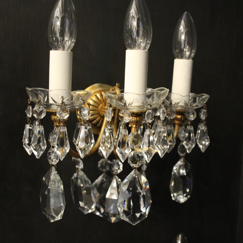 A set of four French triple-arm wall lights with gilt brass frames, candle sleeves, glass drip pans, and clear faceted crystal drops. View III