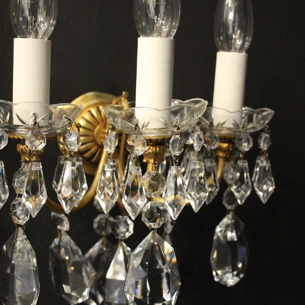 A set of four French triple-arm wall lights with gilt brass frames, candle sleeves, glass drip pans, and clear faceted crystal drops. View IV