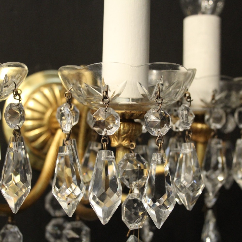 A set of four French triple-arm wall lights with gilt brass frames, candle sleeves, glass drip pans, and clear faceted crystal drops. View V