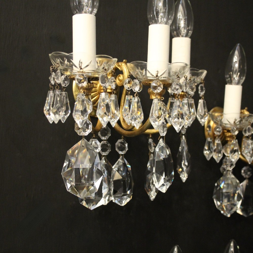 A set of four French triple-arm wall lights with gilt brass frames, candle sleeves, glass drip pans, and clear faceted crystal drops. View VI