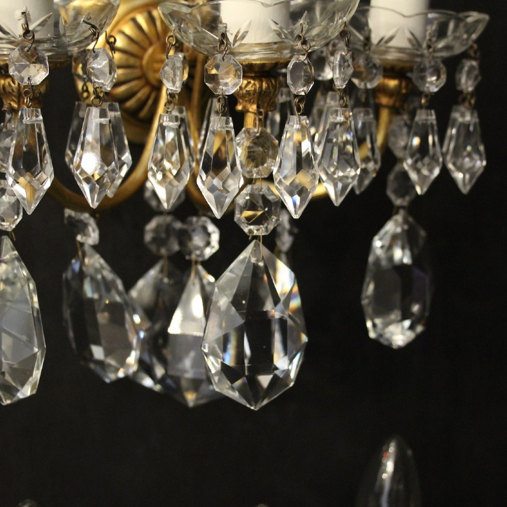 A set of four French triple-arm wall lights with gilt brass frames, candle sleeves, glass drip pans, and clear faceted crystal drops. View VIII