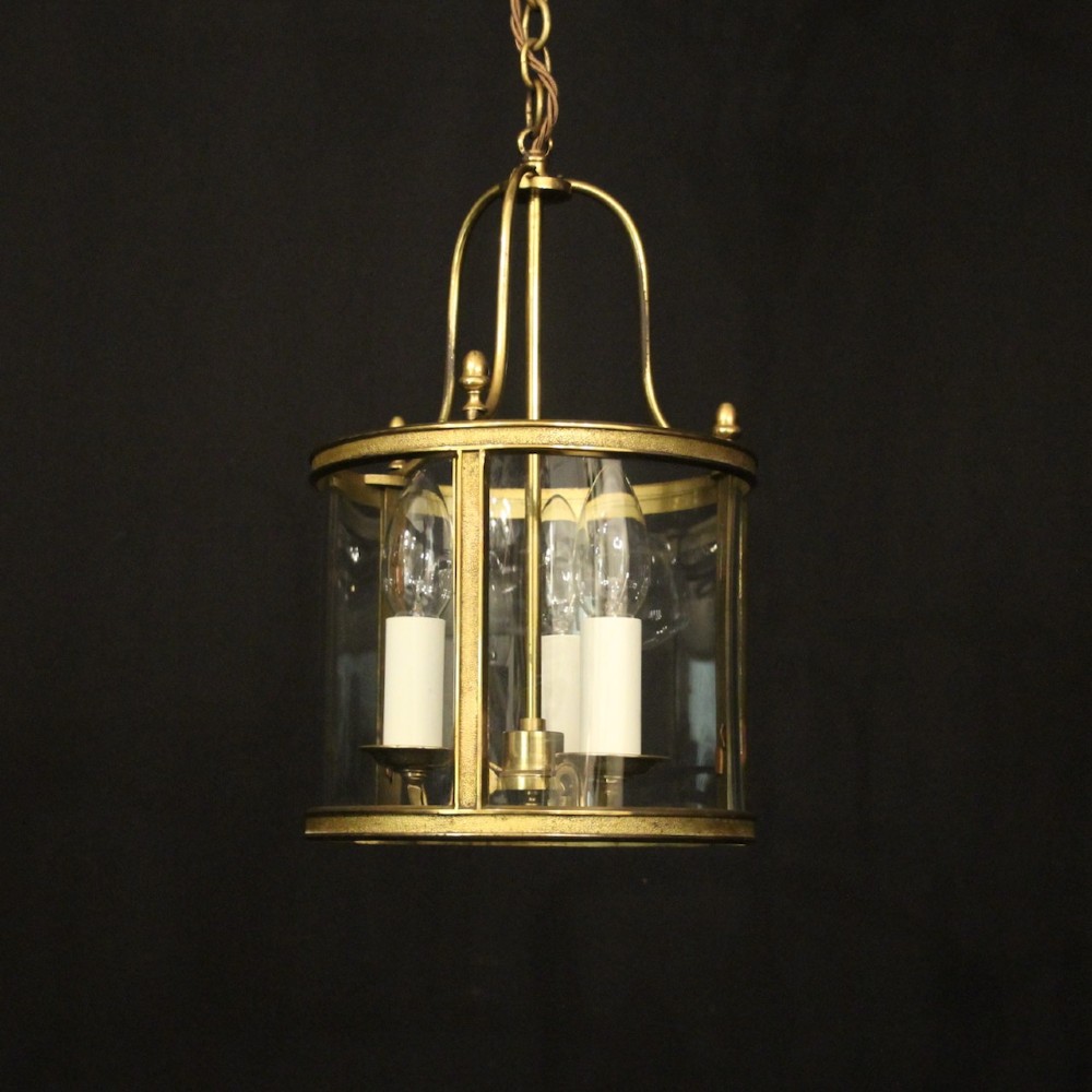 A French gilded brass hall lantern featuring a cylindrical glass shade enclosing three candle-style bulb holders suspended by an arched frame.
