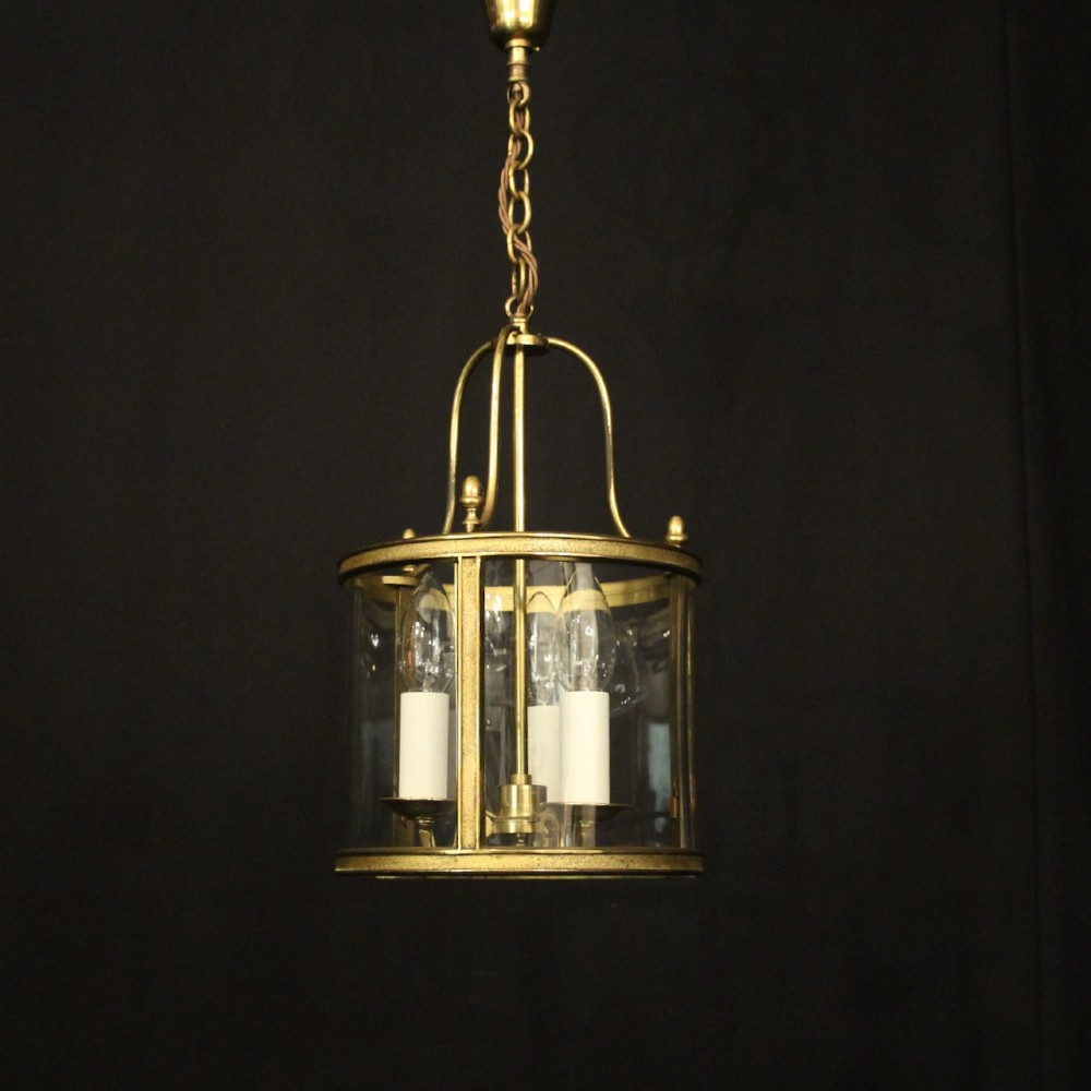 A French gilded brass hall lantern featuring a cylindrical glass shade enclosing three candle-style bulb holders suspended by an arched frame. View II