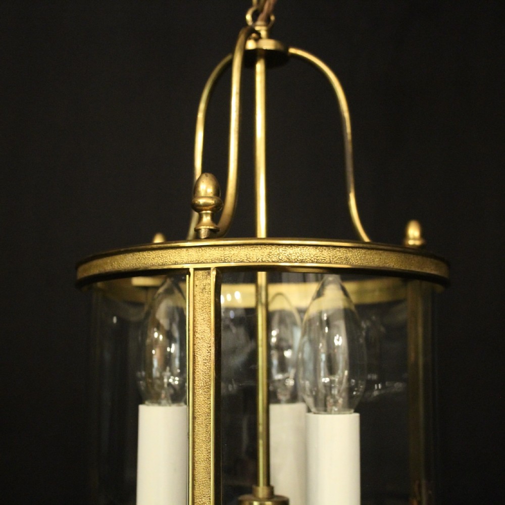 A French gilded brass hall lantern featuring a cylindrical glass shade enclosing three candle-style bulb holders suspended by an arched frame. View IV