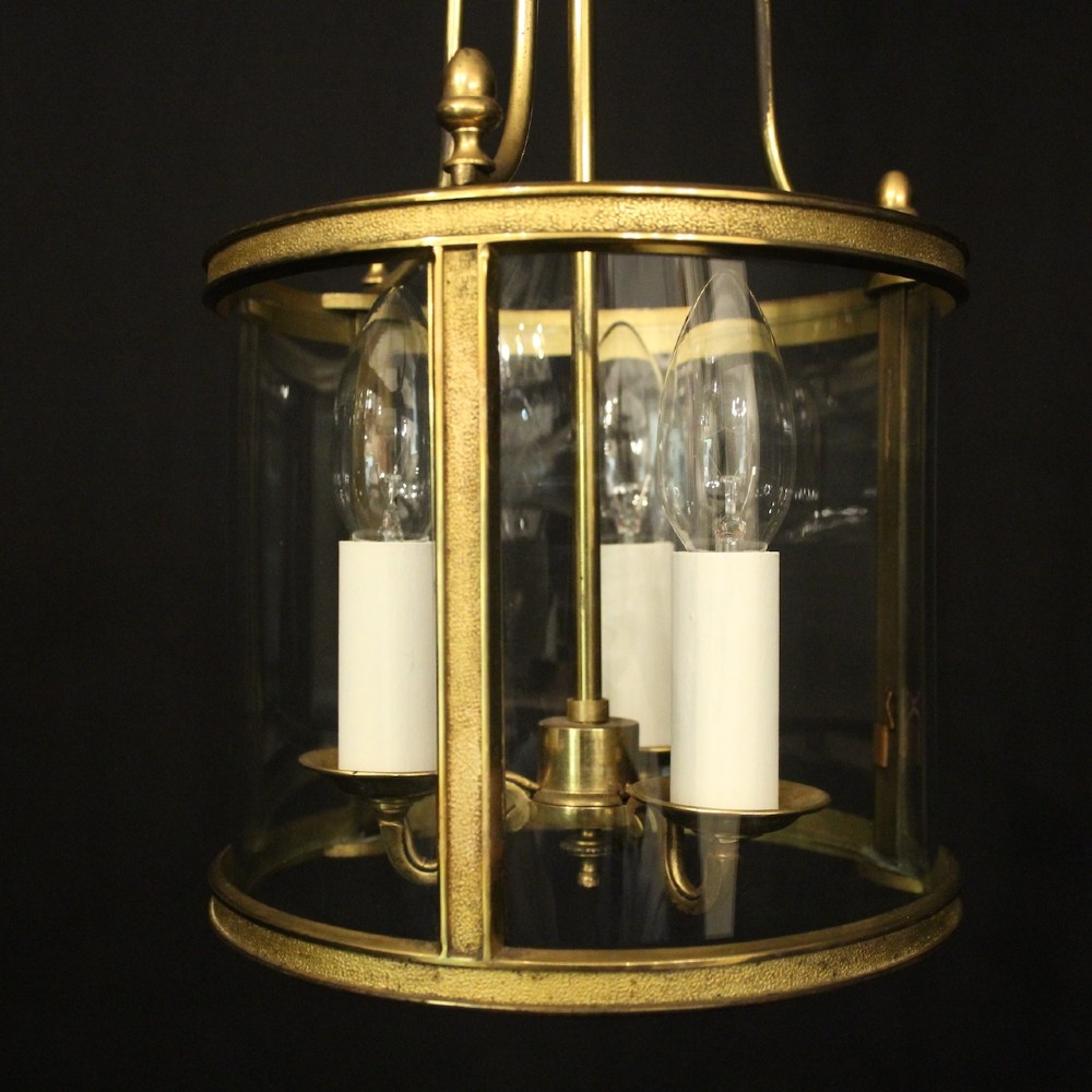 A French gilded brass hall lantern featuring a cylindrical glass shade enclosing three candle-style bulb holders suspended by an arched frame. View V