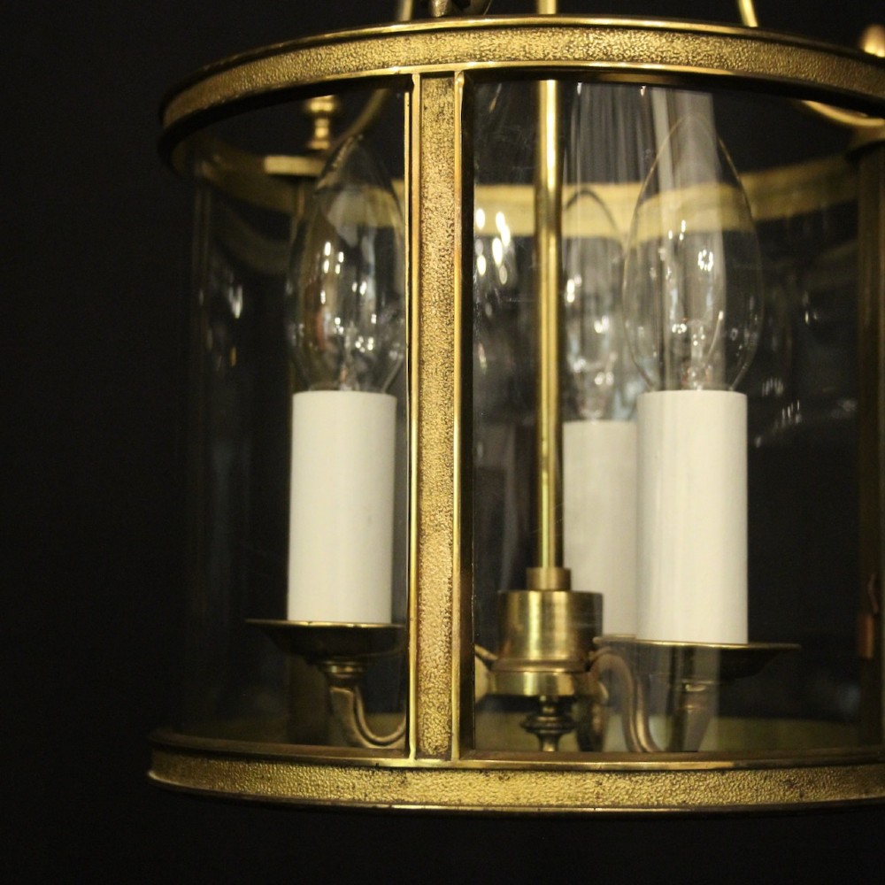 A French gilded brass hall lantern featuring a cylindrical glass shade enclosing three candle-style bulb holders suspended by an arched frame. View VI