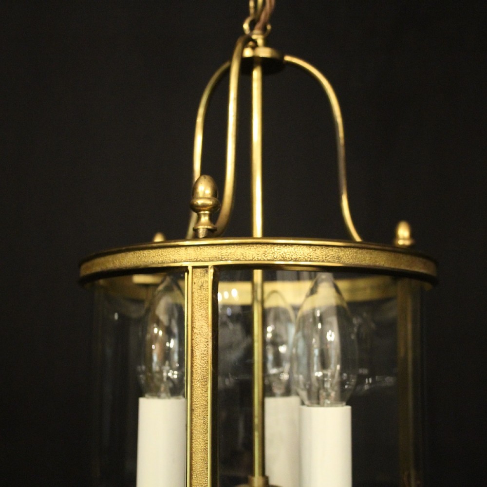 A French gilded brass hall lantern featuring a cylindrical glass shade enclosing three candle-style bulb holders suspended by an arched frame. View VII