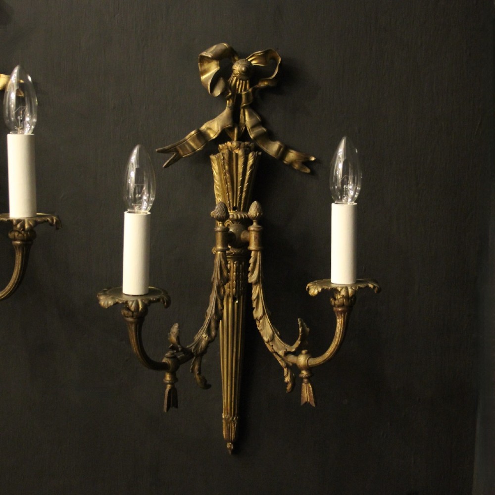 A pair of French gilt bronze two-light wall sconces featuring ribbon bow crestings and fluted tapering backplates mounted on a dark background. View II