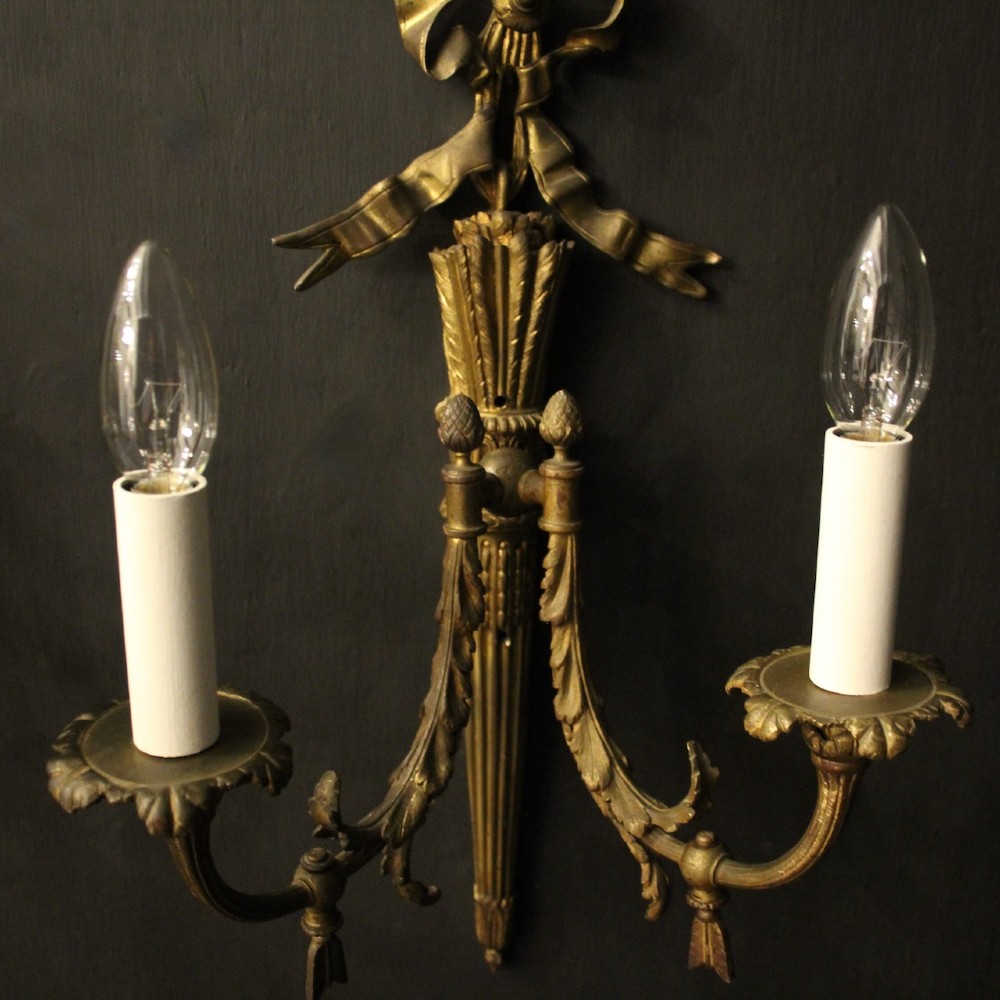 A pair of French gilt bronze two-light wall sconces featuring ribbon bow crestings and fluted tapering backplates mounted on a dark background. View V