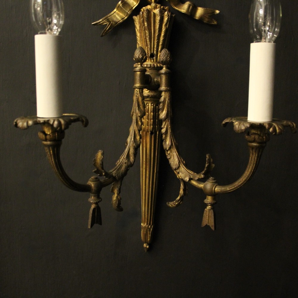 A pair of French gilt bronze two-light wall sconces featuring ribbon bow crestings and fluted tapering backplates mounted on a dark background. View VI