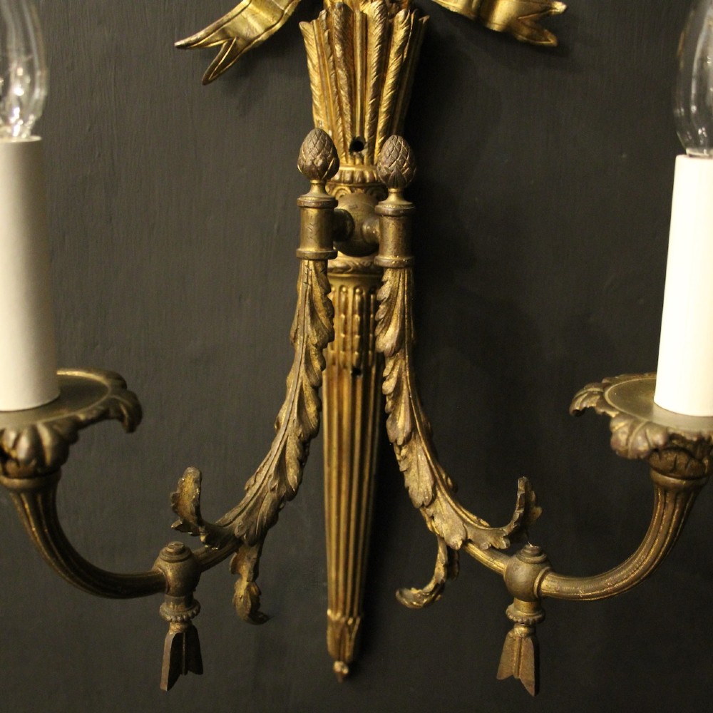 A pair of French gilt bronze two-light wall sconces featuring ribbon bow crestings and fluted tapering backplates mounted on a dark background. View VII