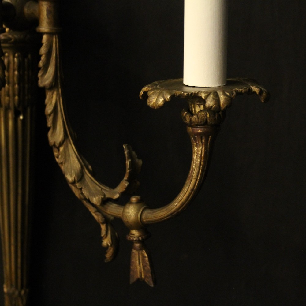 A pair of French gilt bronze two-light wall sconces featuring ribbon bow crestings and fluted tapering backplates mounted on a dark background. View VIII